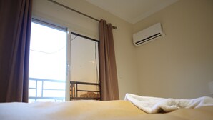 Habitación de hotel con cama, unidad de aire acondicionado, ventana con cortinas y vista a un balcón.