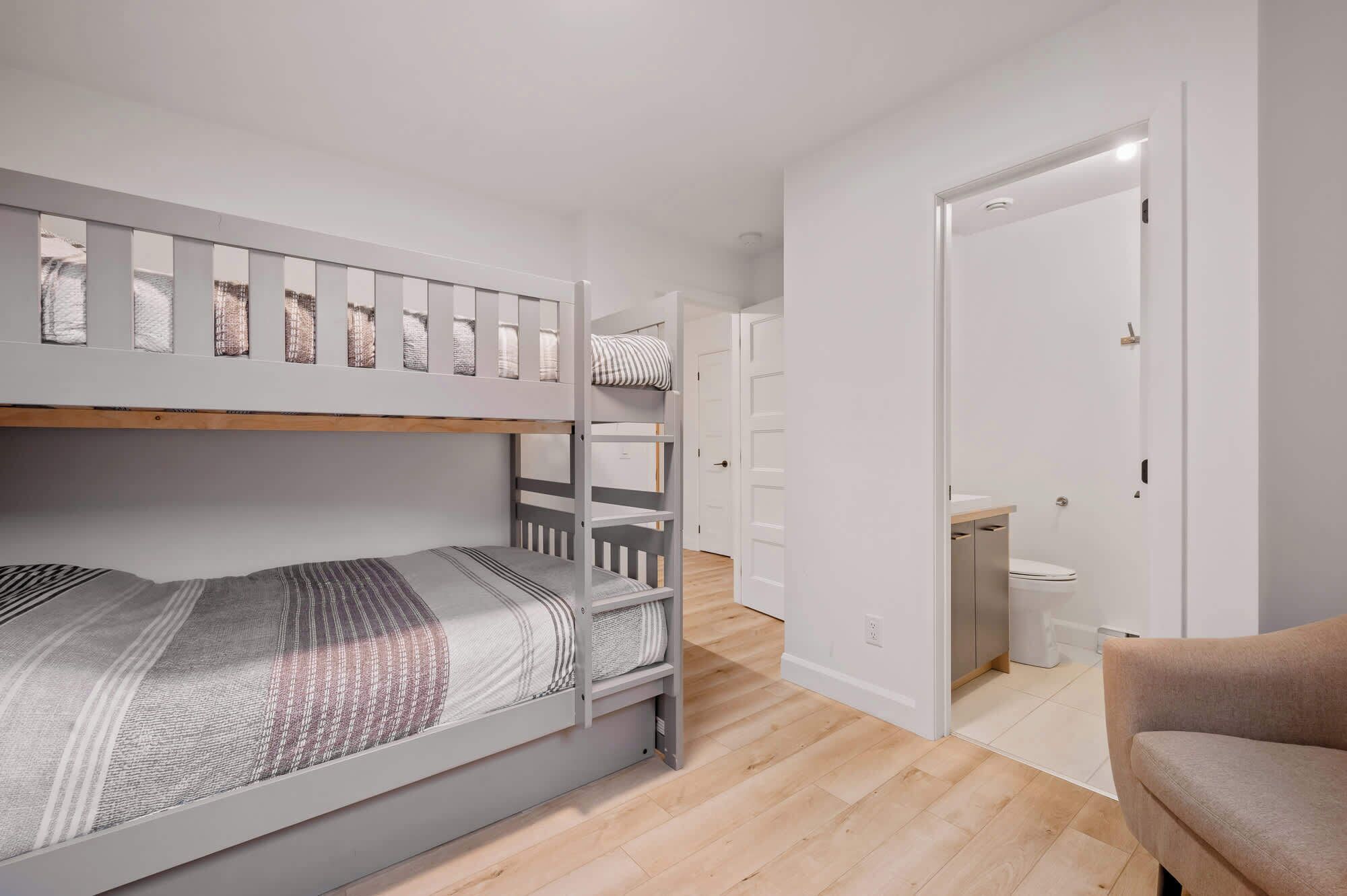 A room with a bunk bed, a small bathroom with a toilet, and a chair.
