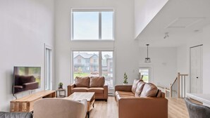 A spacious living room with a large window, a wooden coffee table, a sofa, and a TV on a wooden stand.