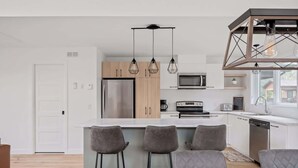 A modern kitchen with a central island, bar stools, and pendant lighting.