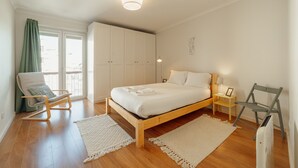 A bedroom with a wooden bed, a chair, a nightstand, and a view of the outside.
