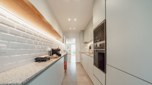 A modern kitchen with white cabinetry, a granite countertop, and a wooden backsplash.