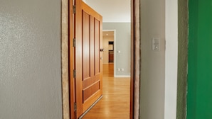 A hallway with a wooden door leading to a room with a white wall and a green accent wall.