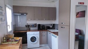 A compact kitchen with a washing machine, a coffee maker, and cabinets. - Cosy house near the sea (Hermanville-sur-Mer)