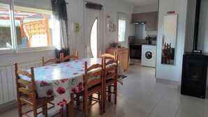 A dining area with a table and chairs, a kitchen with a washing machine, and a fireplace. - Cosy house near the sea (Hermanville-sur-Mer)