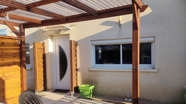 A covered patio area with a wooden pergola, a door, a window, and a green chair. - Cosy house near the sea (Hermanville-sur-Mer)