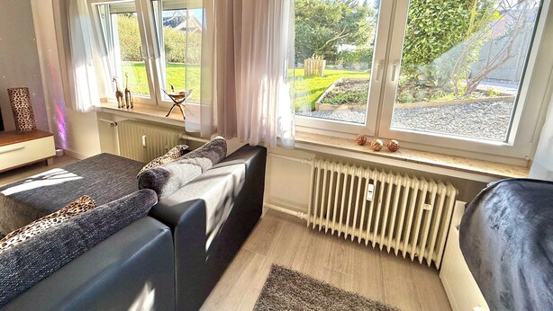 Ein modernes Schlafzimmer mit einem großen Bett, einer Couch und einem Gartenblick durch große Fenster.