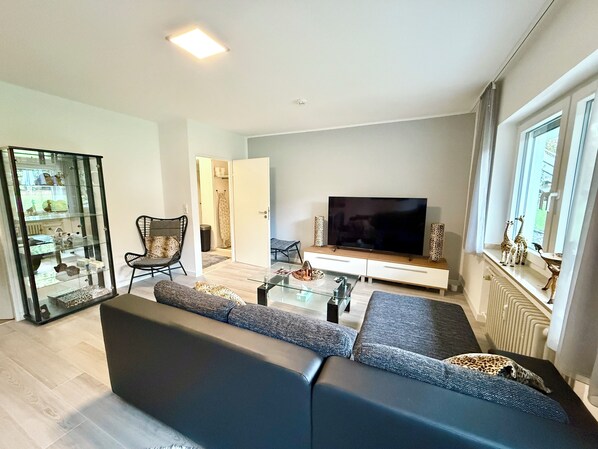 A modern living room with a sectional sofa, a glass coffee table, a flat-screen TV, and a glass display cabinet.