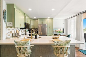Een moderne keuken met groene kastjes, roestvrijstalen apparatuur en een centraal eiland met barstoelen.