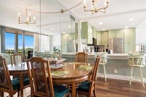 A modern kitchen with a dining area, featuring a large island, wooden chairs, and a view through the window.