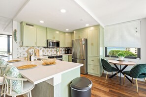 Una cocina moderna con armarios verdes, electrodomésticos de acero inoxidable y una mesa de comedor de madera con sillas.