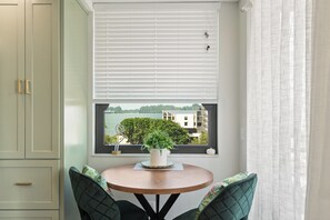 Een kamer met een erker, een ronde tafel en twee stoelen met groene kussens.