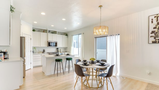 A modern kitchen with white cabinets, a central island, and a dining area with a round table and chairs. - 4 Mi to Zions Bank Stadium: Sleek Herriman Retreat (Herriman)