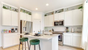 A modern kitchen with white cabinets, a stainless steel refrigerator, a microwave, and a central island with stools. - 4 Mi to Zions Bank Stadium: Sleek Herriman Retreat (Herriman)