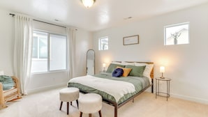 A bedroom with a bed, two stools, a side table, and a window with curtains. - 4 Mi to Zions Bank Stadium: Sleek Herriman Retreat (Herriman)