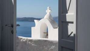 A white building with a dome and a bell tower, viewed through an open door. - Villa Calliope (Santorini)