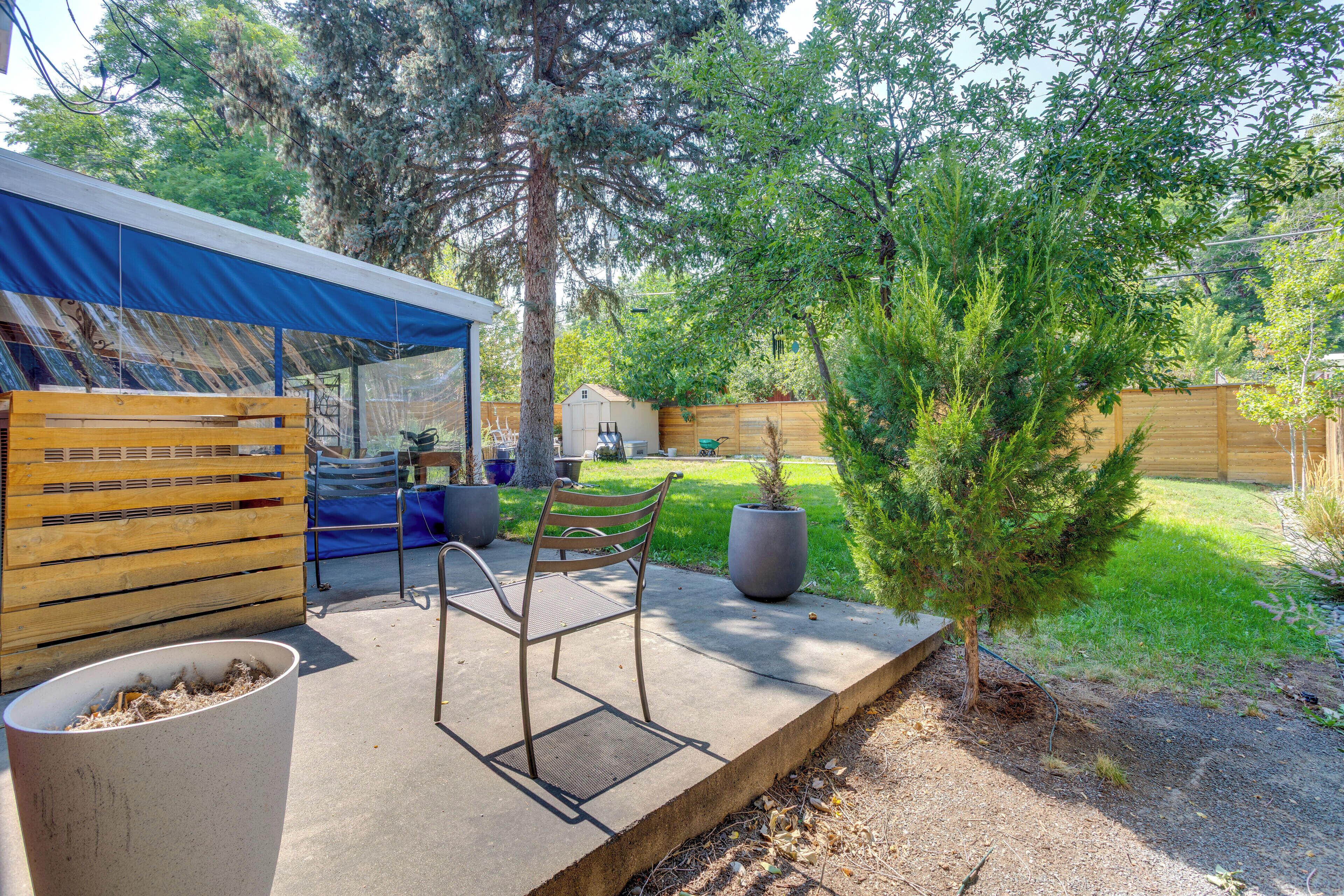 A covered patio area with a wooden bench, a small table, and a trash bin.