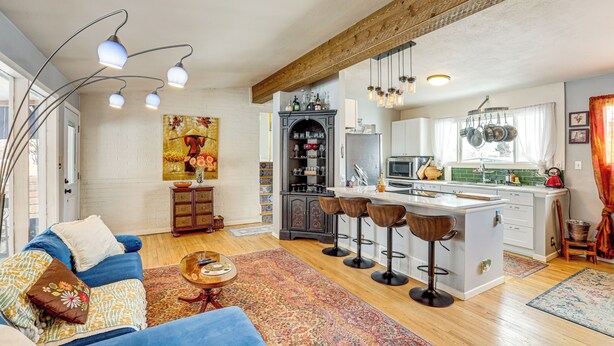 A spacious living area with a sofa, a coffee table, and a kitchen with a bar stool area. - 10 Mi to Red Rocks: Denver Home w/ Fire Pit! (Denver)