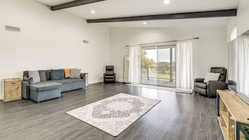 Uma sala de estar ampla com um sofá seccional cinza, uma poltrona de couro preto e uma mesa de centro de madeira.