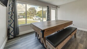 Une pièce avec un banc en bois, une grande fenêtre avec des rideaux et une vue sur une voiture garée à l’extérieur.