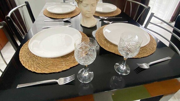 Une table à manger dressée avec de l’argenterie blanche, de la verrerie transparente et un buste décoratif en guise de centre de table.