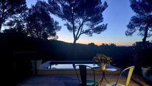 Une terrasse en bois avec deux chaises et une table, donnant sur une piscine et des arbres.