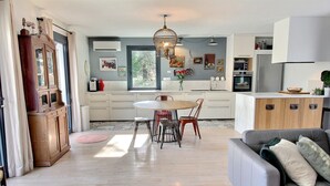 Une cuisine moderne avec des meubles blancs, un coin repas doté d’une table ronde et de chaises, et un canapé gris agrémenté de coussins.