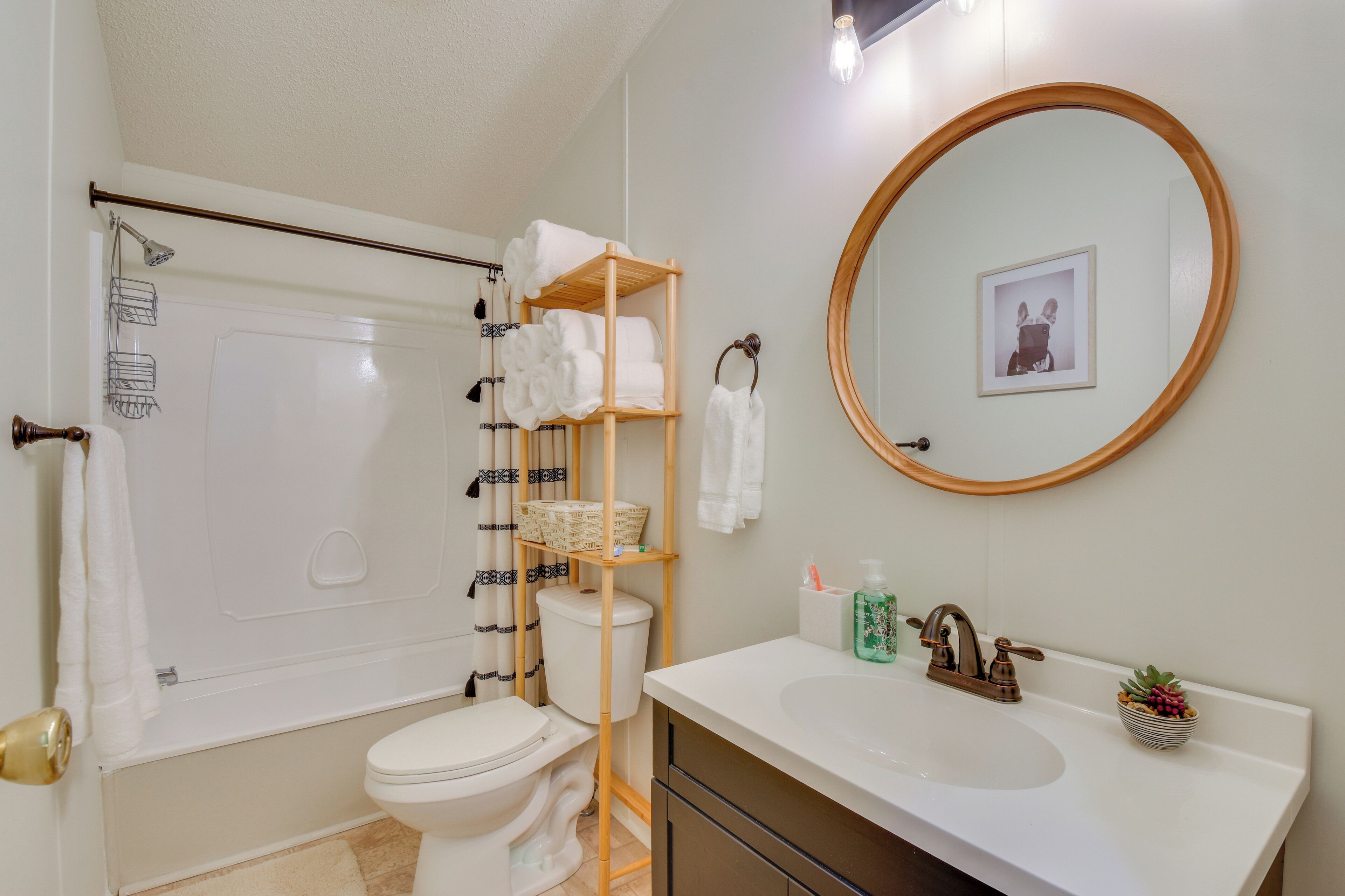 A bathroom with a toilet, shower, and sink. There are shelves with towels and a framed picture on the wall.