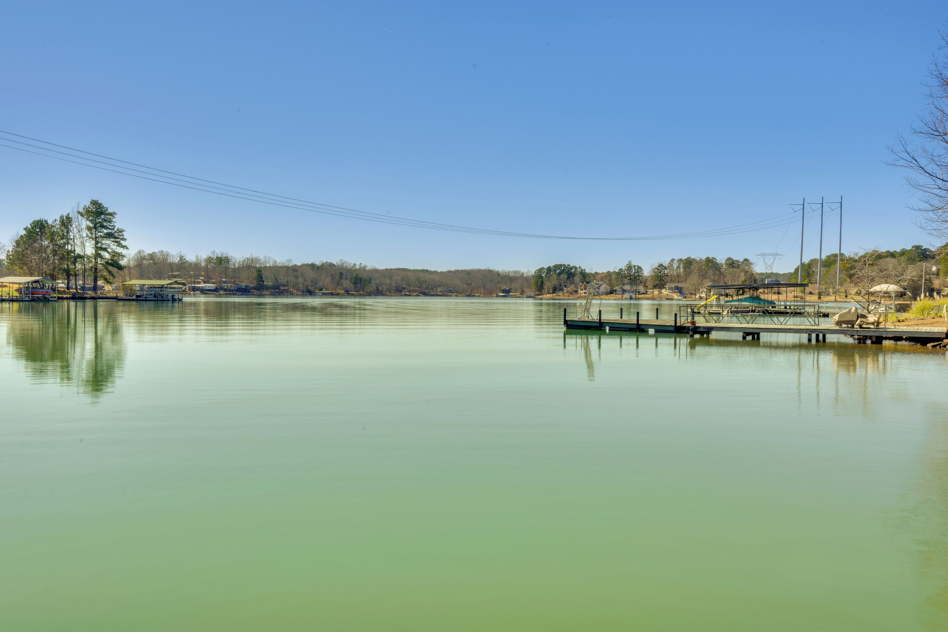 Un lago tranquilo con un muelle y un pequeño edificio, rodeado de árboles y cielos despejados.