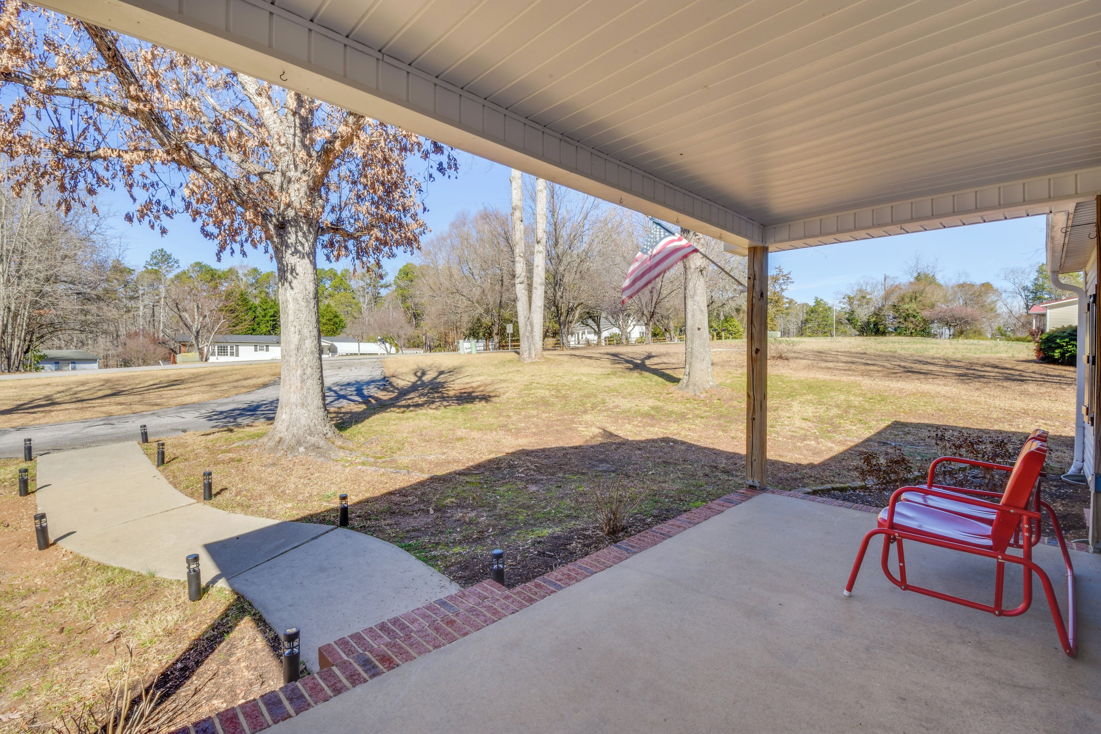 A covered patio with a red metal bench, a flagpole with an American flag, and a tree with autumn leaves.