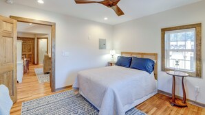 A bedroom with a bed, wooden floor, ceiling fan, bedside table, lamp, window, and a door leading to another room. - 2 Blocks to Appalachian Trail! Couple's Retreat (Hot Springs)