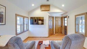 A spacious living area with two grey armchairs, a wooden coffee table with books and a remote control, and a view into the kitchen through an open door. - Walk to Appalachian Trail: Hot Springs Hideaway (Hot Springs)