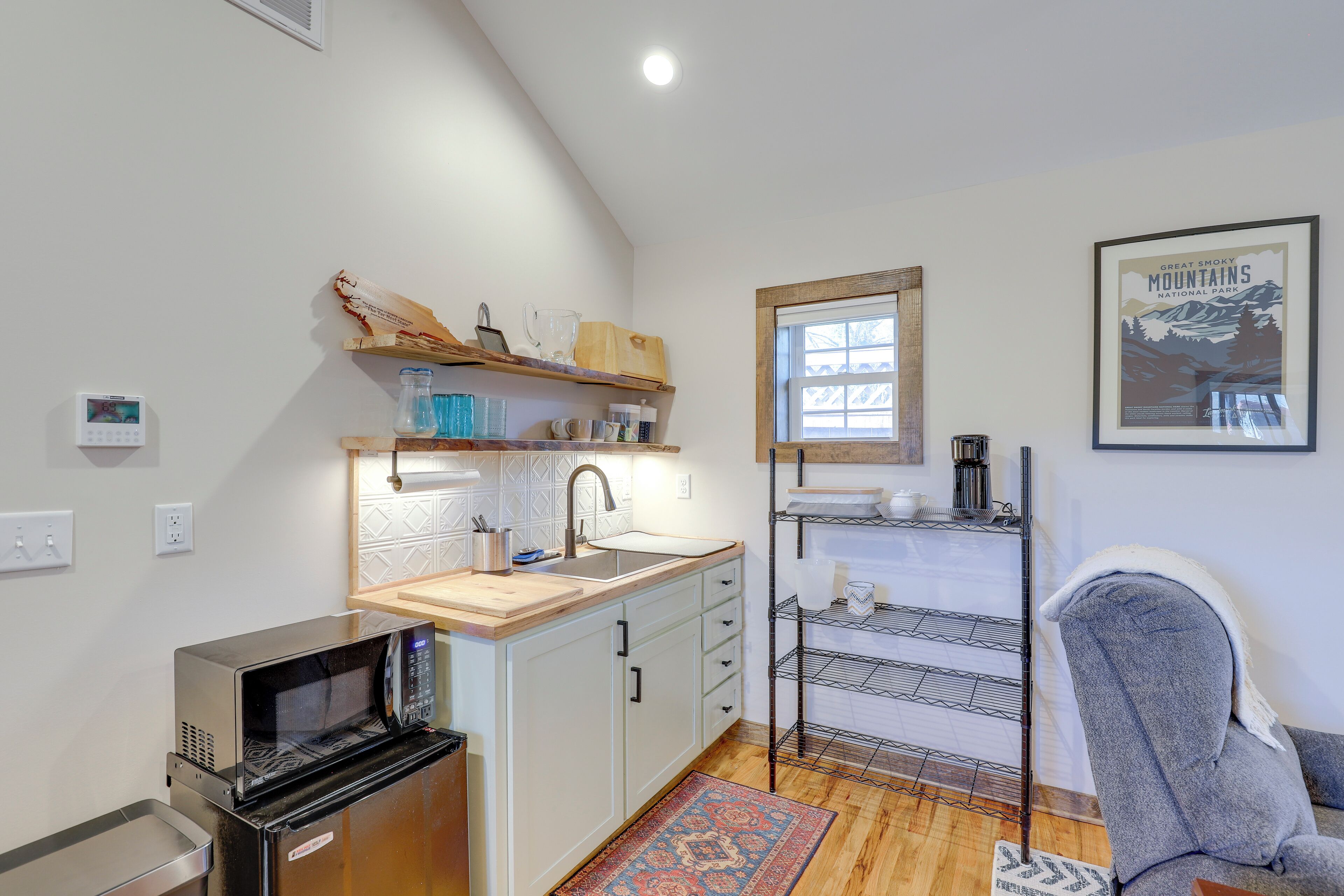 A compact kitchen with a microwave, sink, and wooden shelves.