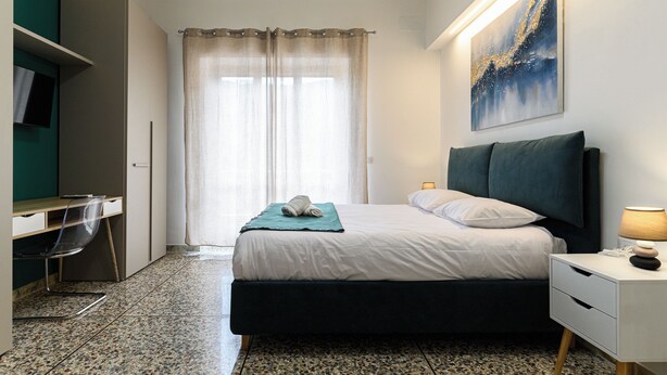 A bedroom with a bed, a desk, a chair, a nightstand, and a painting on the wall. - Rome House Jambokella Apartment in the historic district of Monteverde  (Roma)