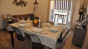A dining area with a table set for six, including plates, cutlery, and glasses. There is a vase with flowers on the table, and a lamp is visible in the background. - Rome House Jambokella Apartment in the historic district of Monteverde  (Roma)
