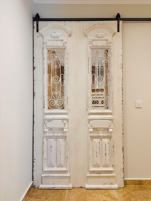 Double doors with ornate metal grilles and decorative moldings lead into a room with a tiled floor.