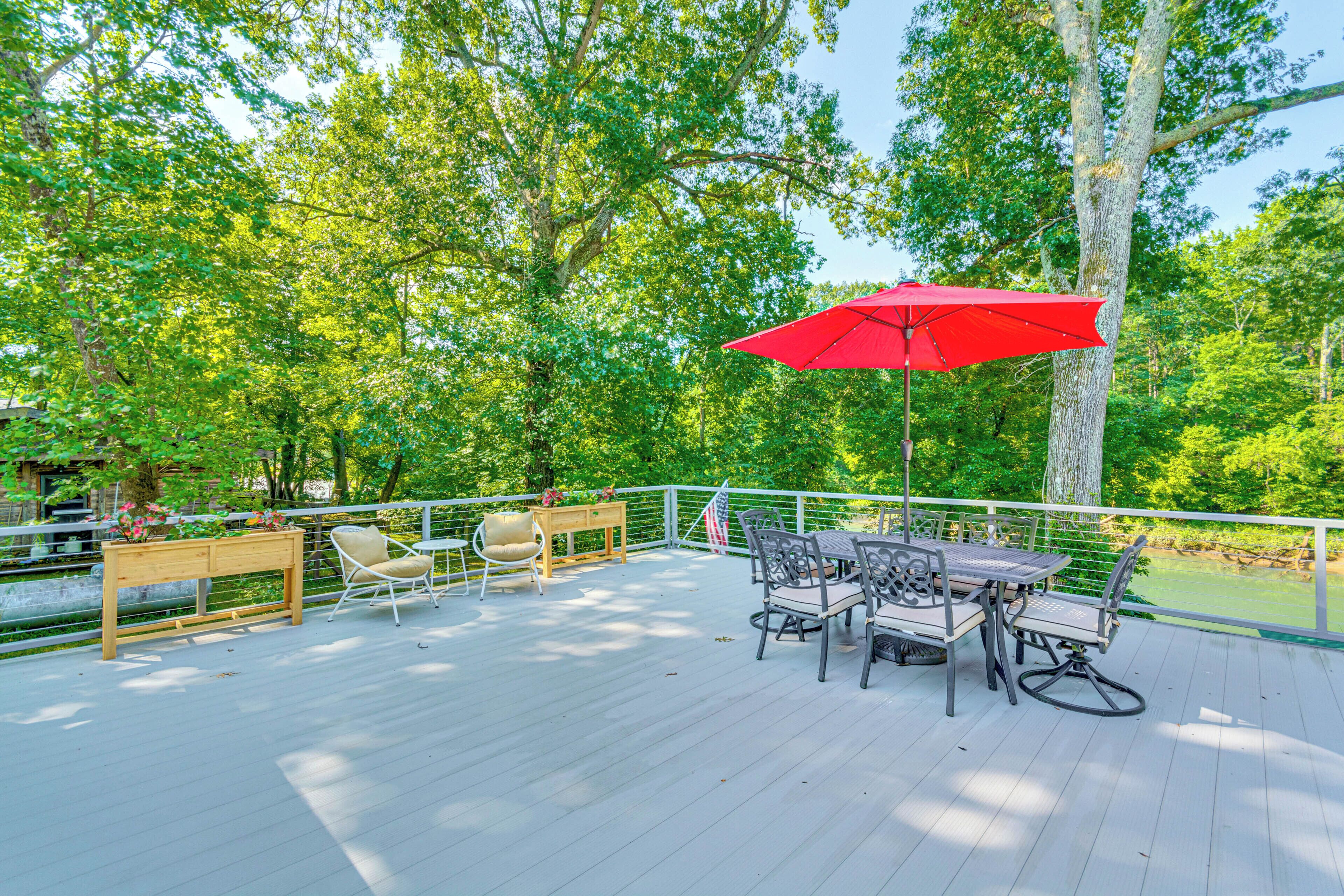 A wooden deck with outdoor furniture, including a table and chairs, and a red umbrella.