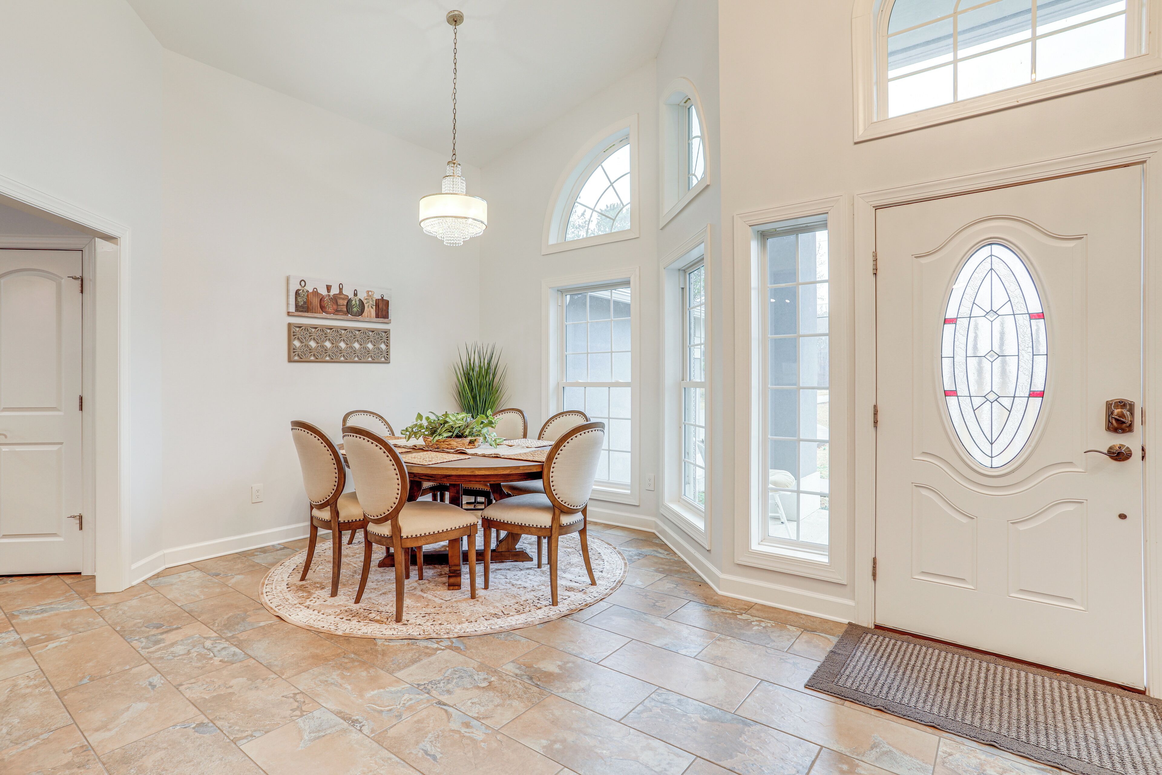 A dining area with a round table, six chairs, and a chandelier.