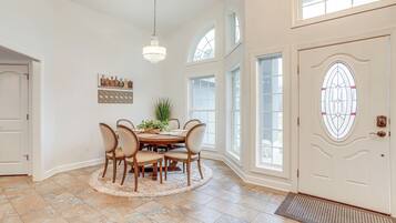 A dining area with a round table, six chairs, and a chandelier.