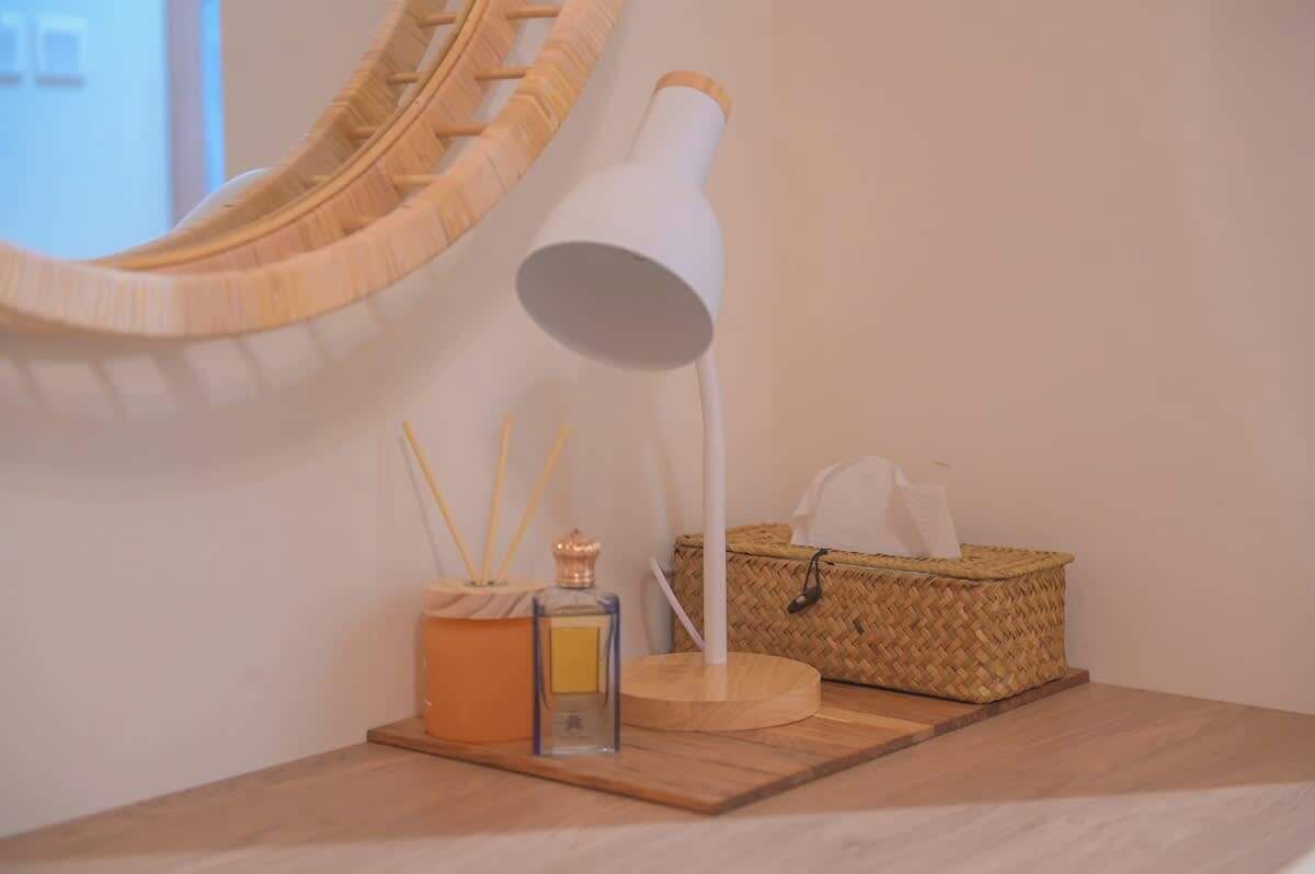 A wooden table with a white lamp, a woven basket, and a small box with a candle and reed diffuser.