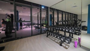Un gimnasio con equipo de ejercicio, incluyendo cintas de correr y mancuernas, y un espejo grande que refleja el interior.