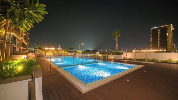 Una piscina en la azotea rodeada de vegetación y edificios modernos al fondo.