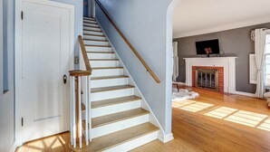 A staircase with wooden steps and a handrail, leading to a room with a fireplace and a television on a mantel. - Half-mi to Unc: Historic Dtwn Greeley Home (Greeley)