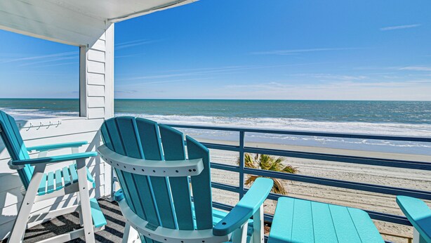 Une terrasse au bord de la plage, avec des fauteuils Adirondack turquoise et une vue sur l’océan.