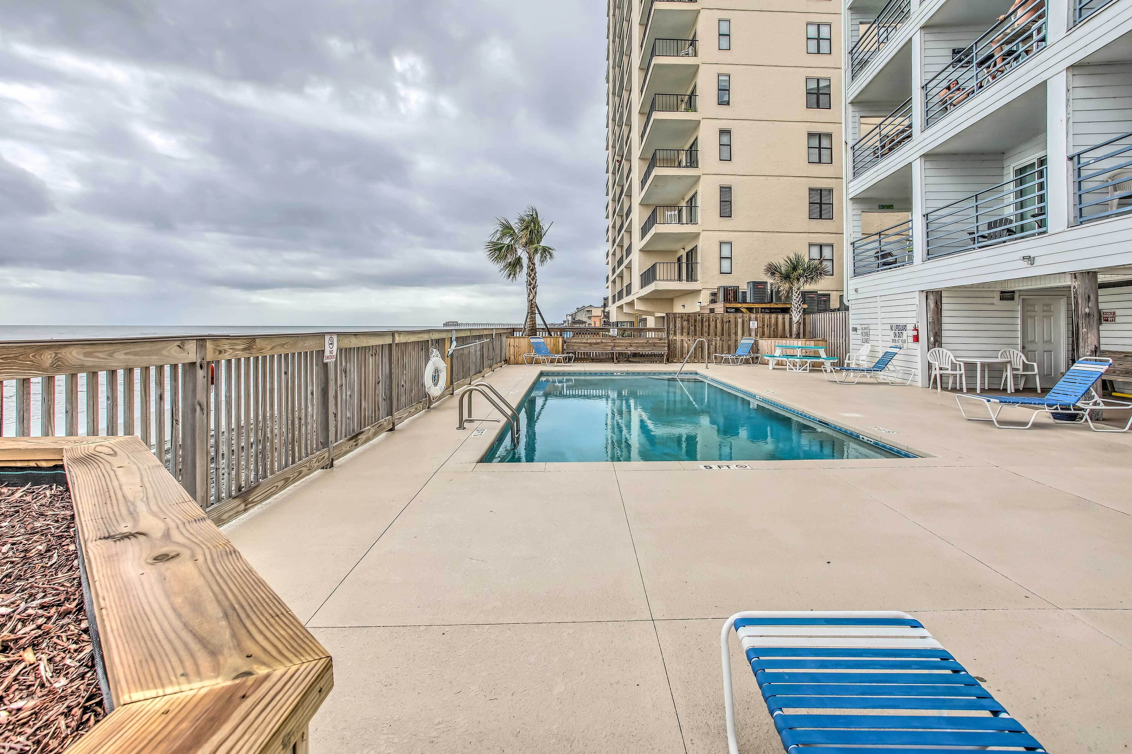 A pool area with a wooden deck, lounge chairs, and a view of a tall building.