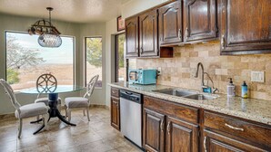 A kitchen with wooden cabinets, a dishwasher, a sink, and a dining area with a glass table and chairs. - Views + Fire Pit: Hilltop Retreat in Rio Rico! (Rio Rico)