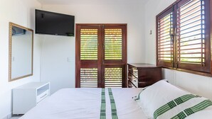 Ein Schlafzimmer mit einem Bett, einem an der Wand montierten Fernseher, einem Kleiderschrank und einem Fenster mit Jalousien.