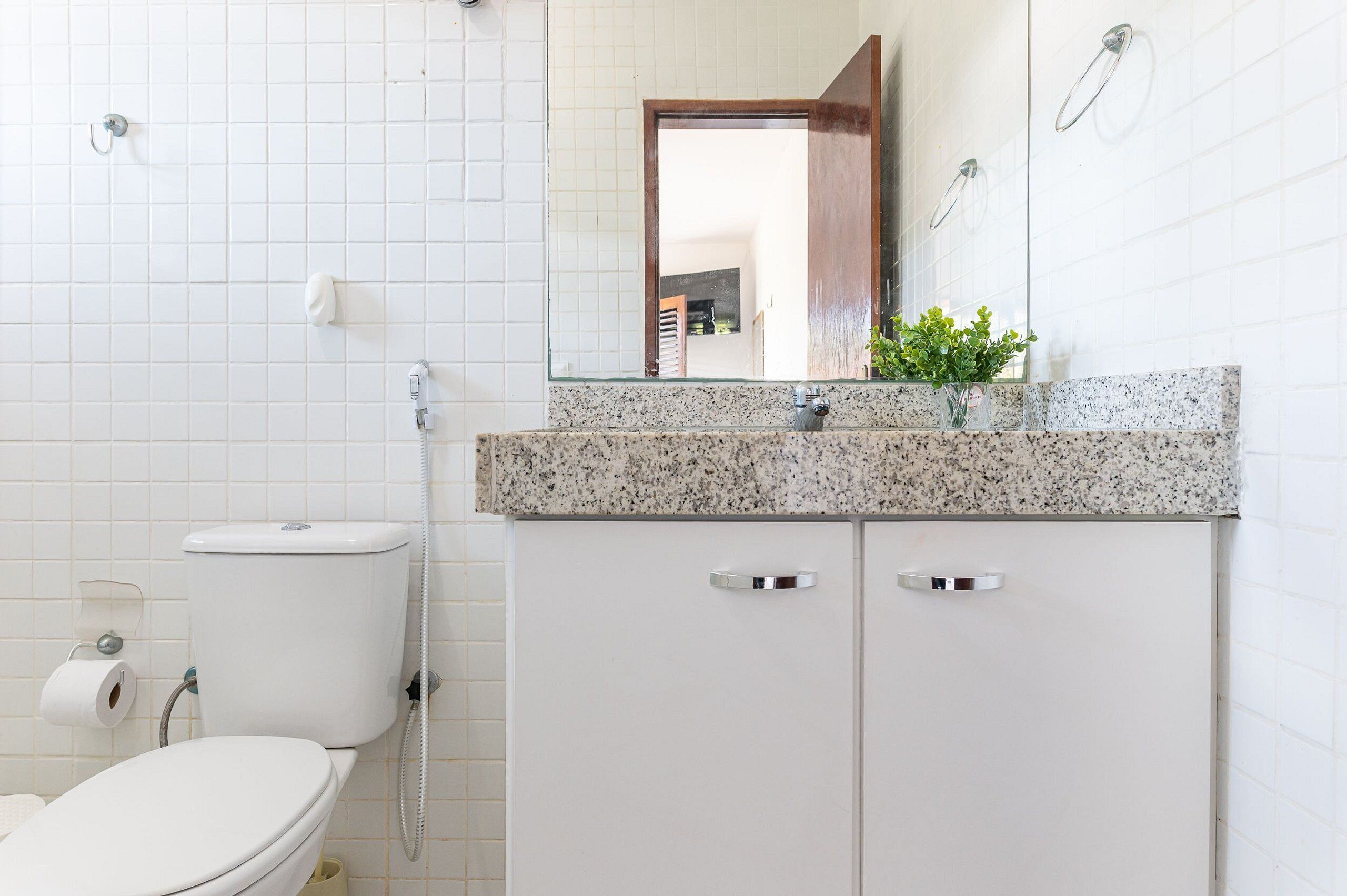 Un baño con inodoro blanco, lavamanos con encimera de granito y espejo sobre el lavamanos.