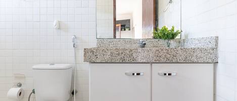 Un baño con inodoro blanco, lavamanos con encimera de granito y espejo sobre el lavamanos.