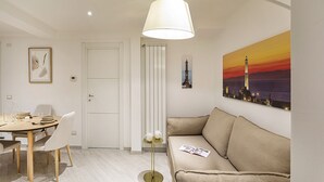 A modern living room with a beige sofa, a dining table with chairs, a floor lamp, and a cityscape painting on the wall. - Galea Studio by Wonderful Italy (Genova)